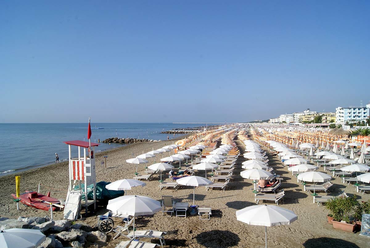 Uitgestrekte witte parasols op een zandstrand direct aan de blauwe zee