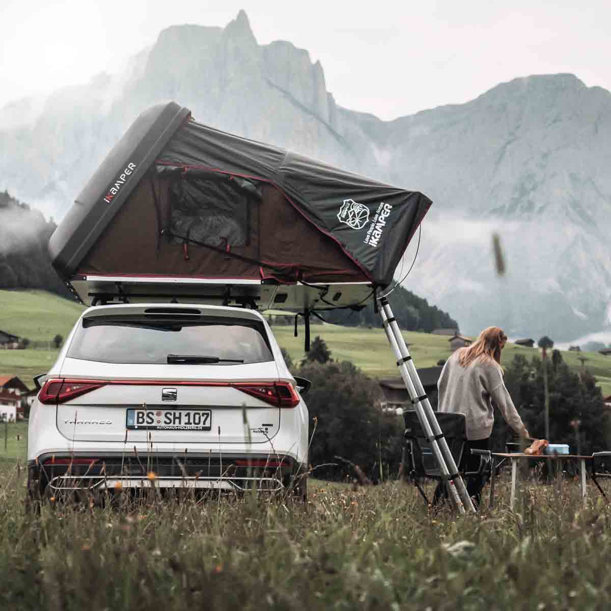 Vrouw staat in de bergen naast haar auto met daktent