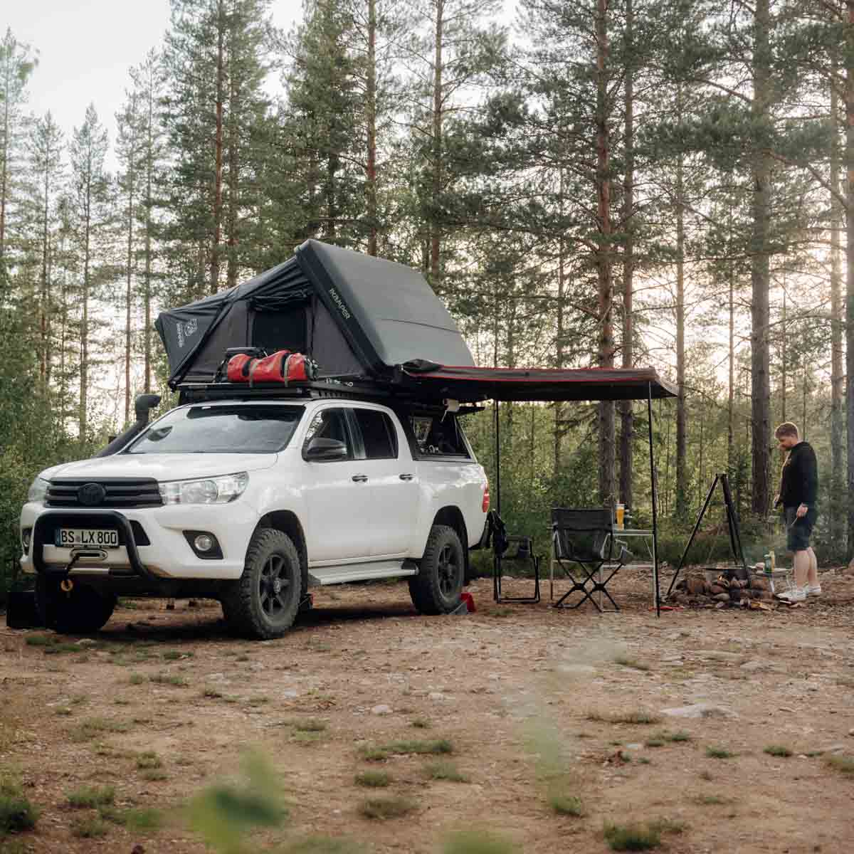 Man kampeert met zijn pickup-truck met daktent en luifel in het bos