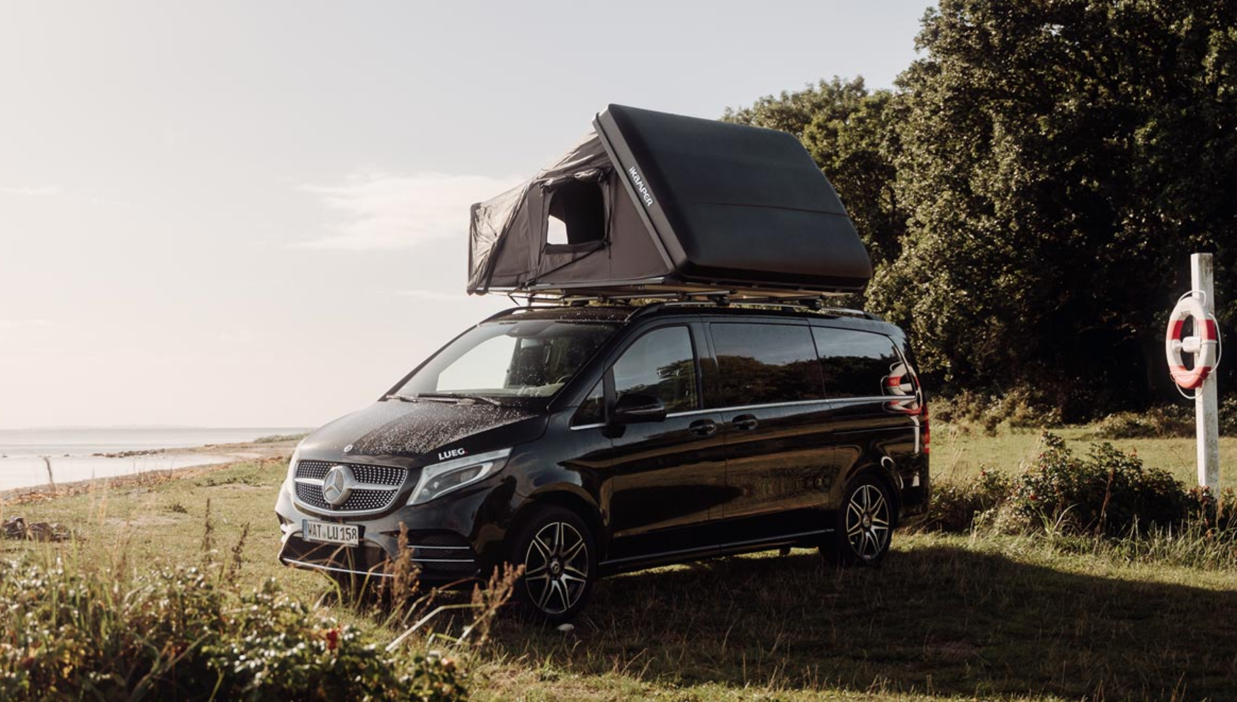 Zwarte auto parkeert aan een meer met opengeklapte harde schaal daktent voor 3 personen
