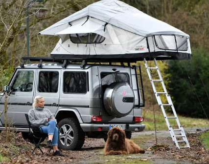 Vrouw zit op een campingstoel met haar hond voor haar auto met Adventure daktent