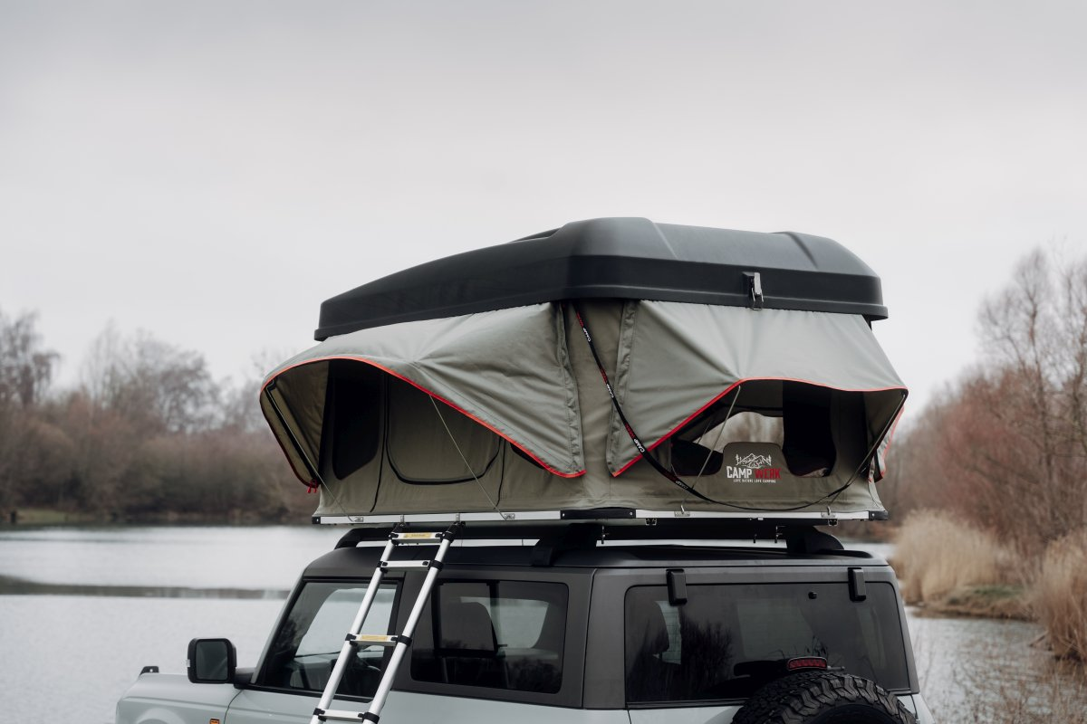 Close-up van een CAMPWERK-daktent op een grijze auto, geparkeerd aan een meer