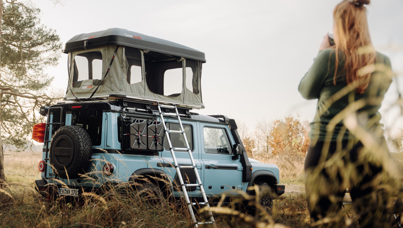 Vrouw drinkt voor haar auto met Good Vibes daktent een kopje koffie