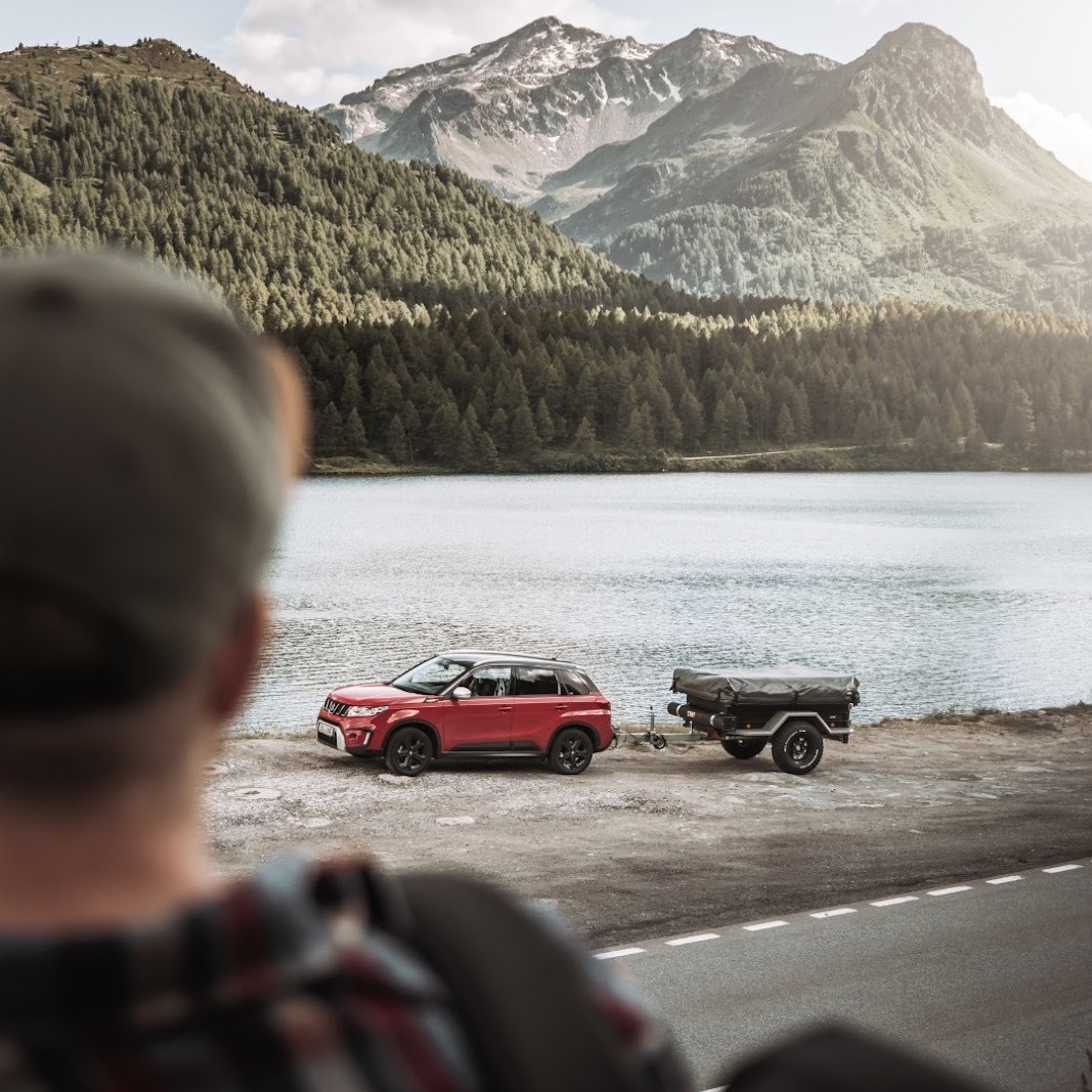 Persoon kijkt naar een auto met afgekoppelde tenttrailer aan het meer