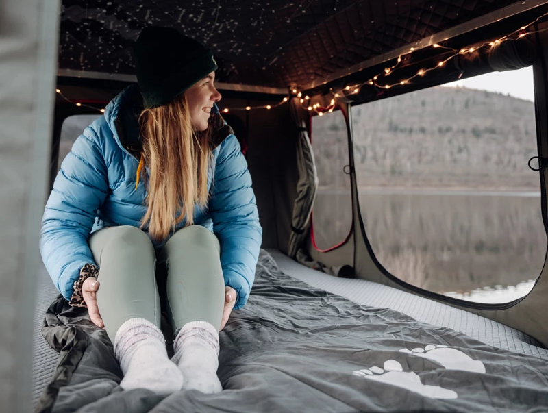 Kampeerder zit op een elektrische deken in haar daktent in de winter